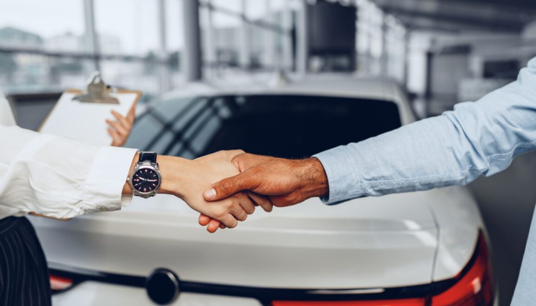 Woman car seller and man car buyer handshaking in car salon building